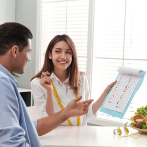 Young,Nutritionist,Consulting,Patient,At,Table,In,Clinic